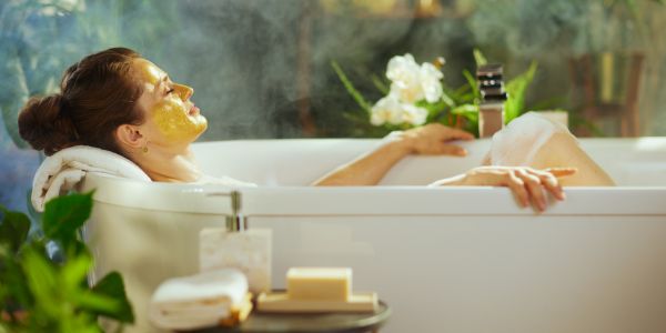 Femme détendue prenant un bain chaud avec un masque visage, illustrant un rituel d’auto-soin à la ménopause pour apaiser le stress, renforcer l’immunité et retrouver l’équilibre intérieur.