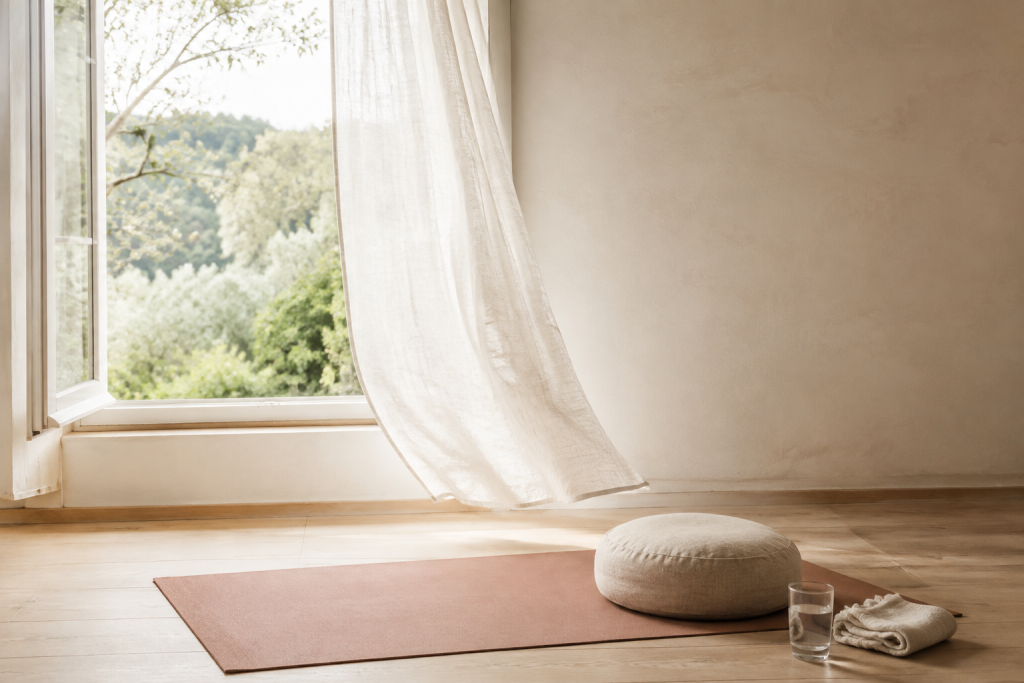 Tapis de yoga et coussin de méditation près d’une fenêtre ouverte pour apaiser le stress à la ménopause.